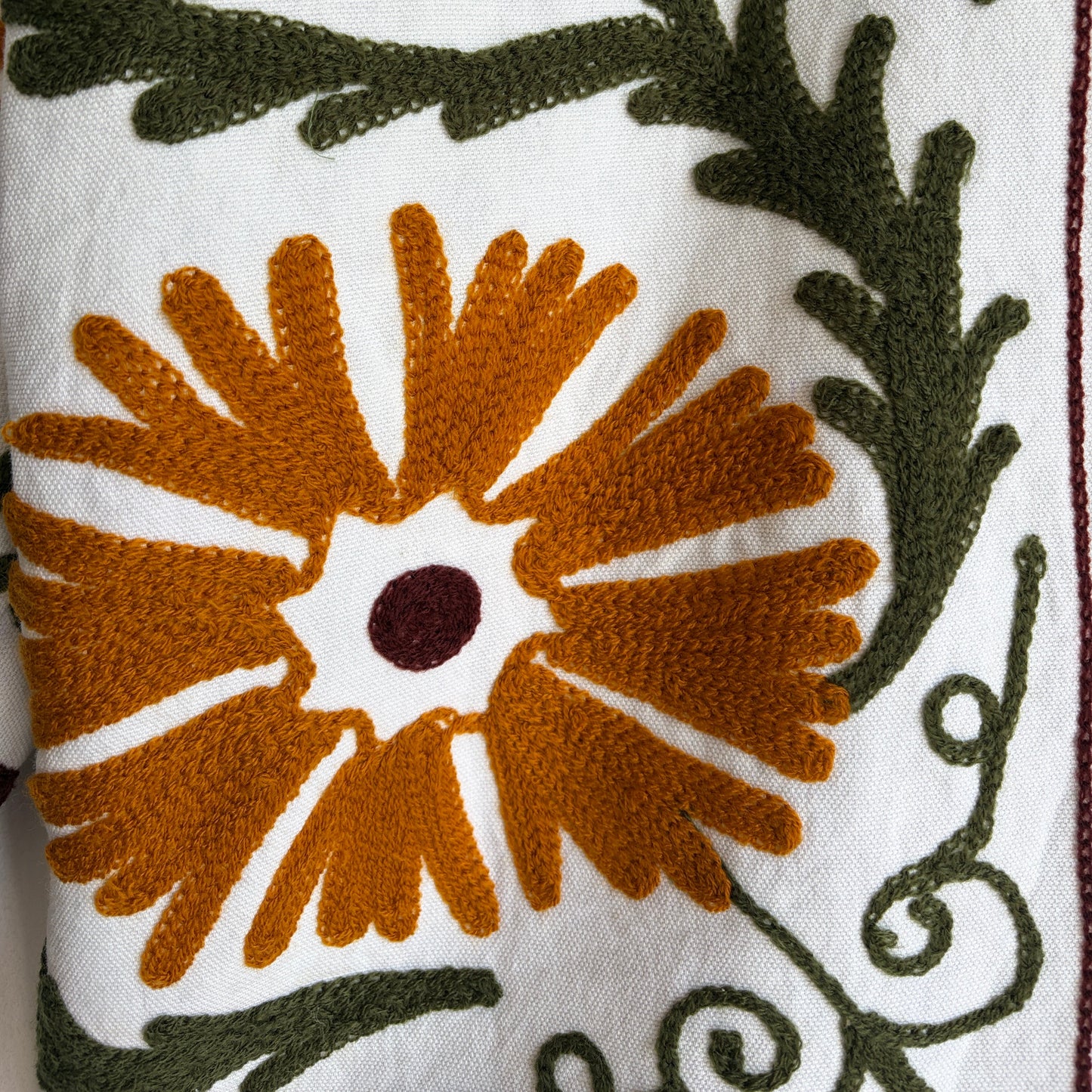 white cotton jacket with a colorful suzani embroidered floral and geometric pattern in brown, orange, and green. 