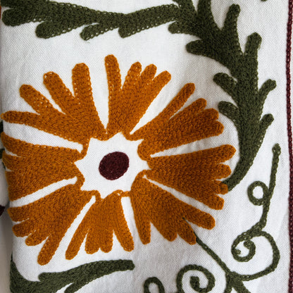 white cotton jacket with a colorful suzani embroidered floral and geometric pattern in brown, orange, and green. 