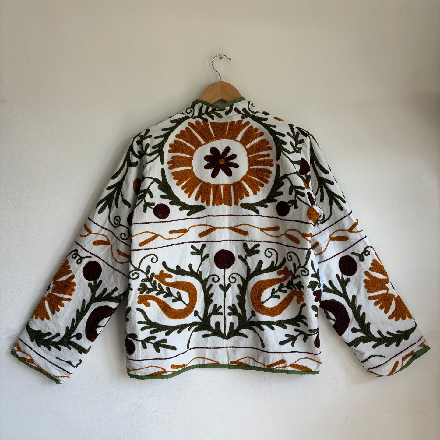 white cotton jacket with a colorful suzani embroidered floral and geometric pattern in brown, orange, and green. 
