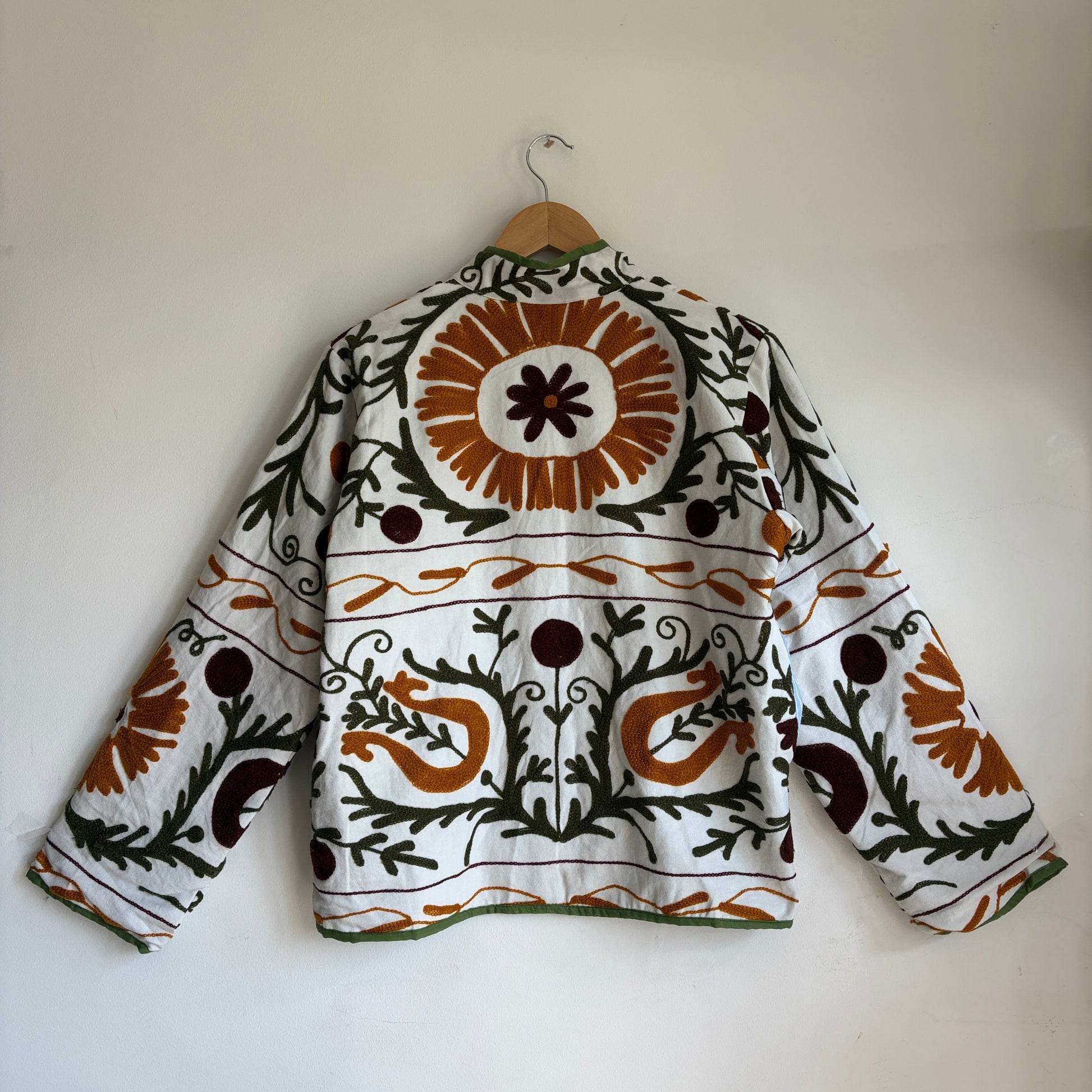 white cotton jacket with a colorful suzani embroidered floral and geometric pattern in brown, orange, and green. 