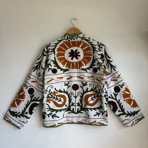 white cotton jacket with a colorful suzani embroidered floral and geometric pattern in brown, orange, and green. 