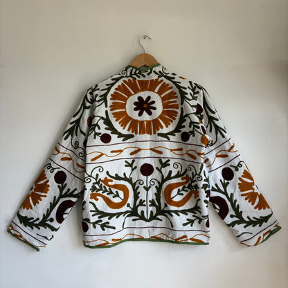 white cotton jacket with a colorful suzani embroidered floral and geometric pattern in brown, orange, and green. 