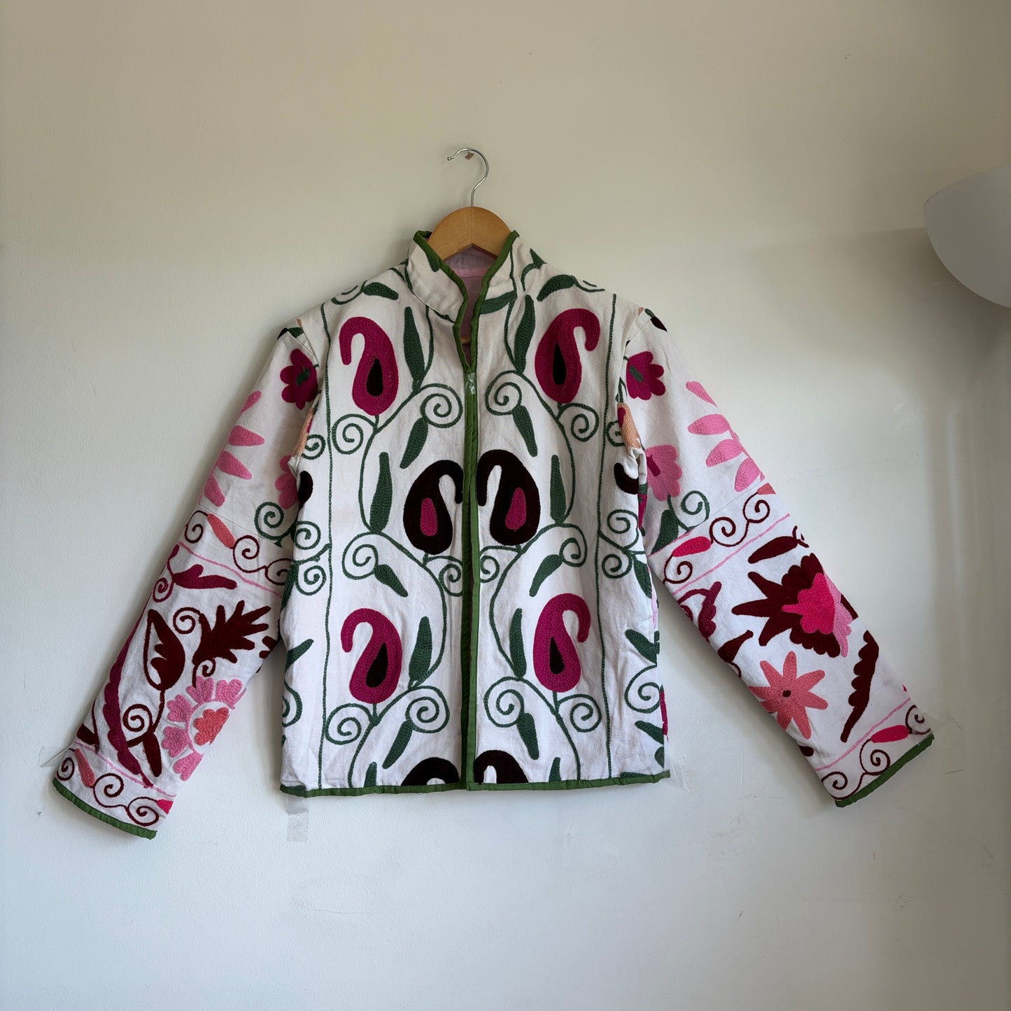 White quilted jacket with pink, green, and black embroidered paisley and floral patterns. 