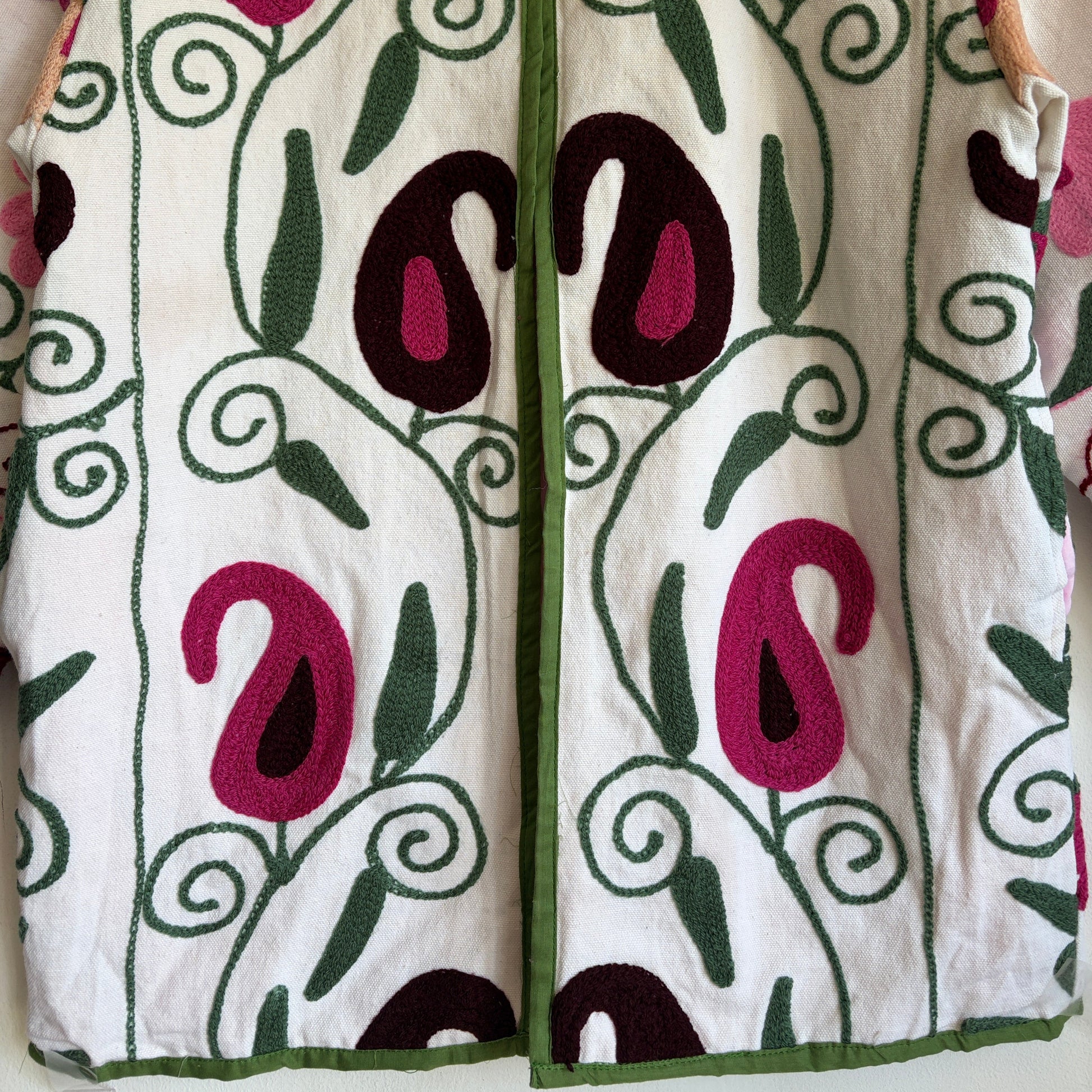 White quilted jacket with pink, green, and black embroidered paisley and floral patterns. 