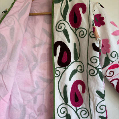 White quilted jacket with pink, green, and black embroidered paisley and floral patterns. 