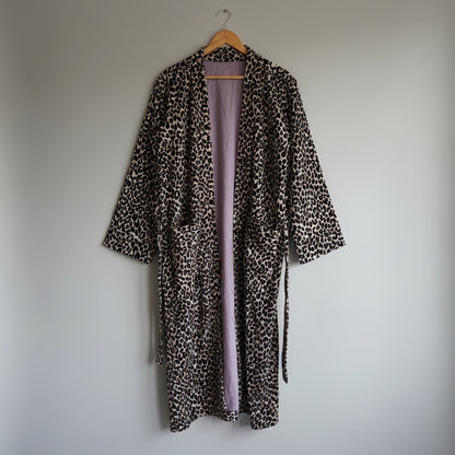 A leopard print robe hanging on a hanger against a plain white wall. 