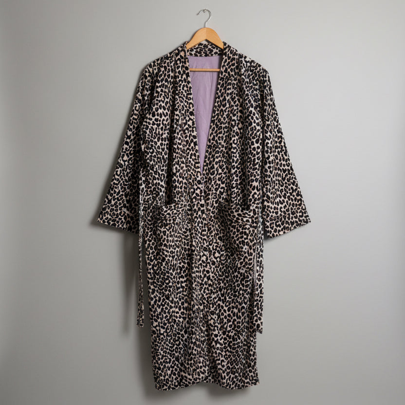 A leopard print robe hanging on a wooden hanger against a plain white wall
