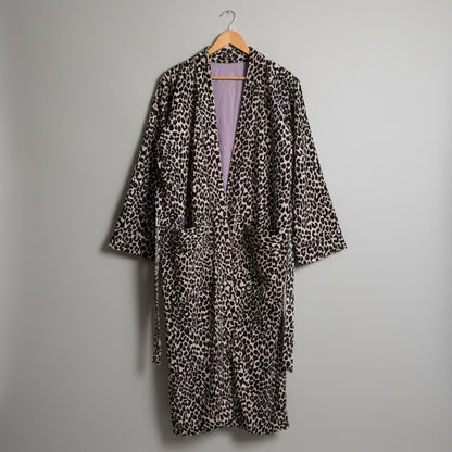 A leopard print robe hanging on a wooden hanger against a plain white wall