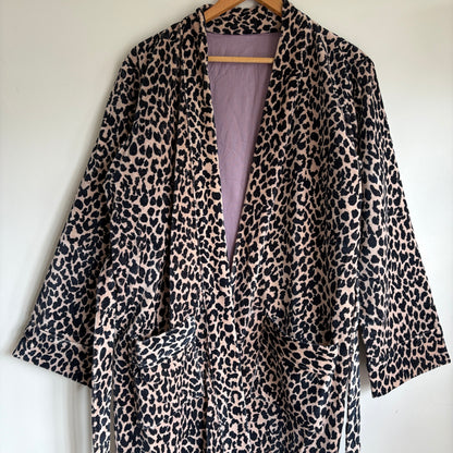 A leopard print robe hanging on a hanger against a plain white wall. 