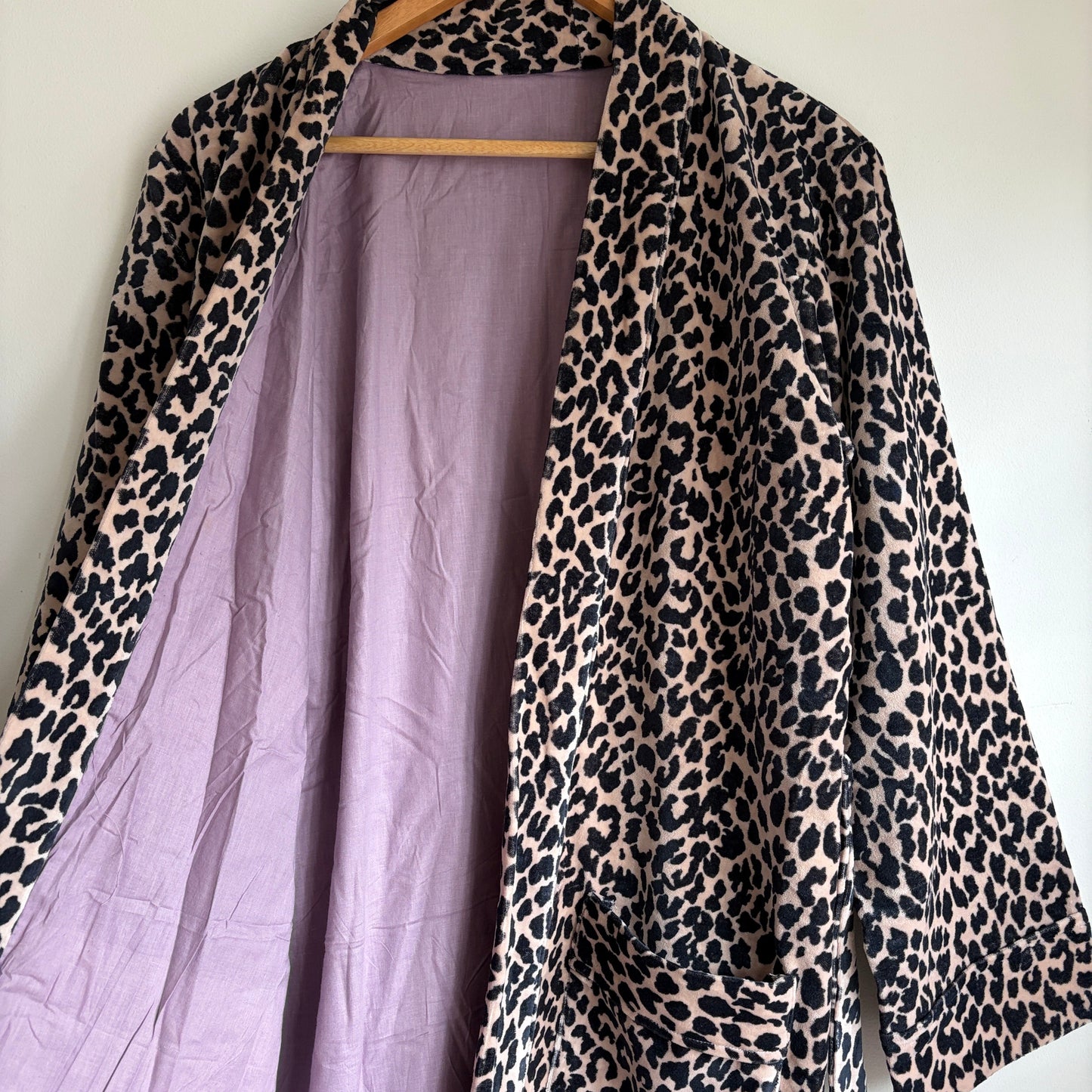 A leopard print robe hanging on a hanger against a plain white wall. 