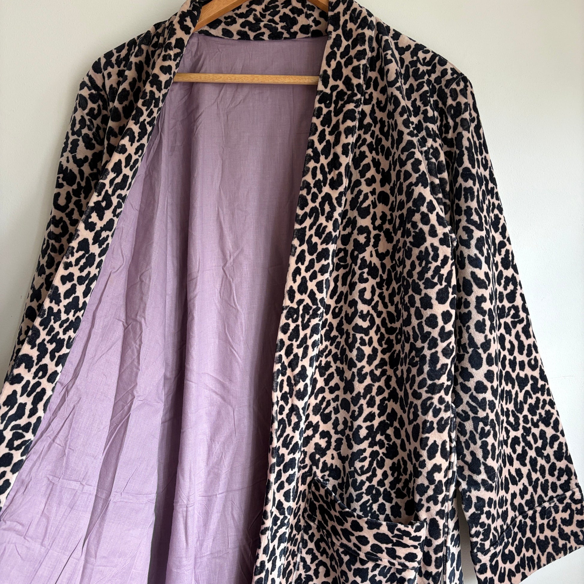 A leopard print robe hanging on a hanger against a plain white wall. 