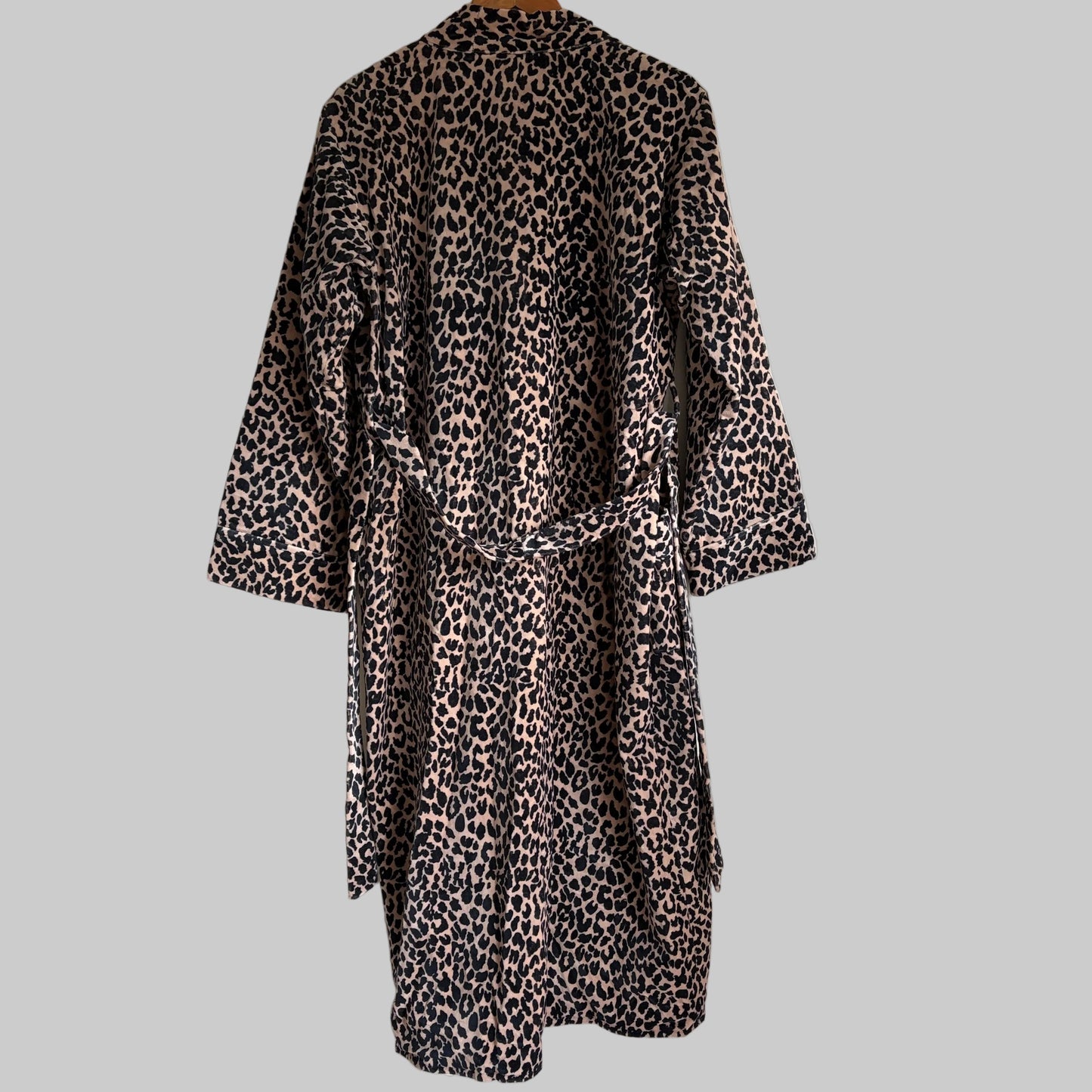 A leopard print robe hanging on a hanger against a plain white wall. 