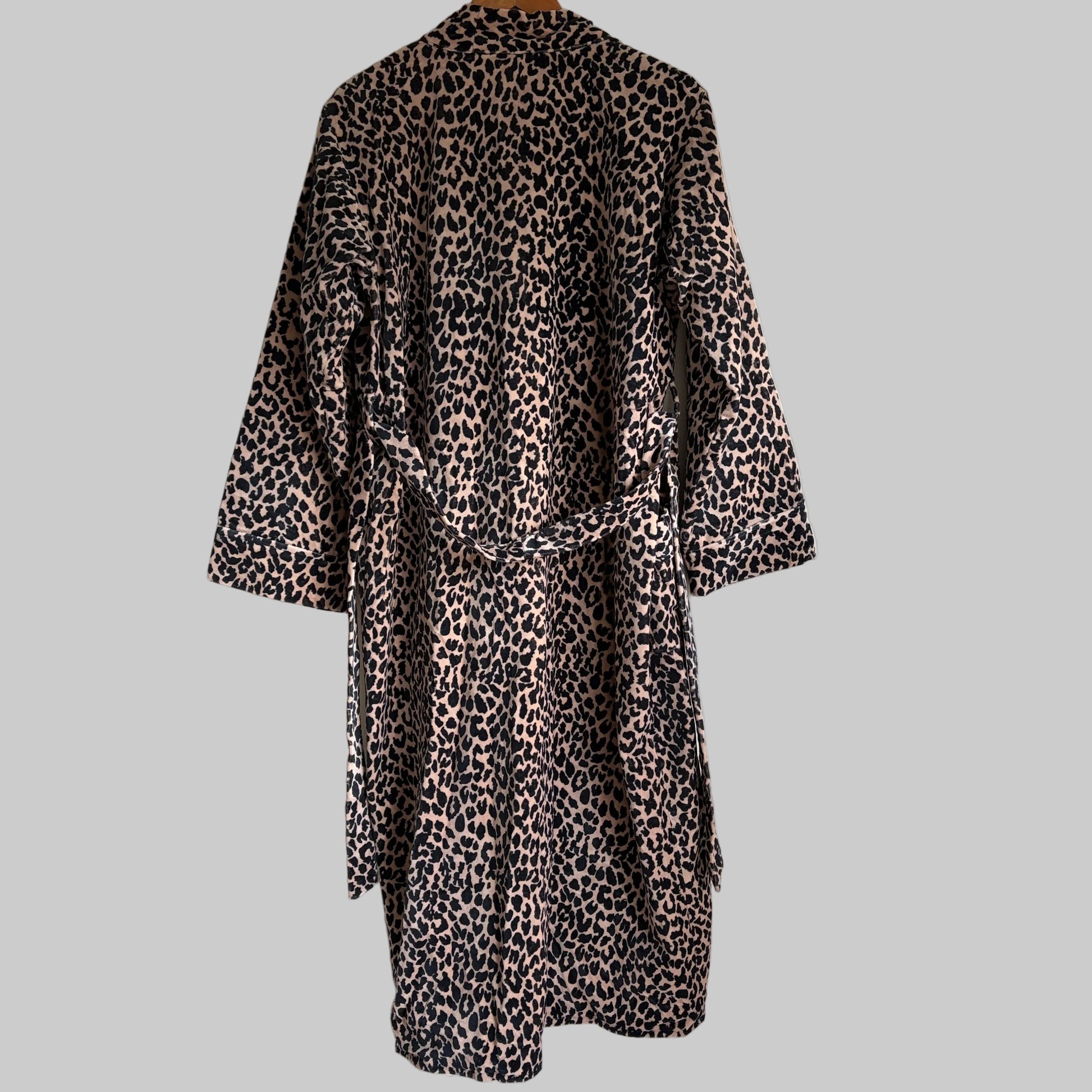 A leopard print robe hanging on a hanger against a plain white wall. 