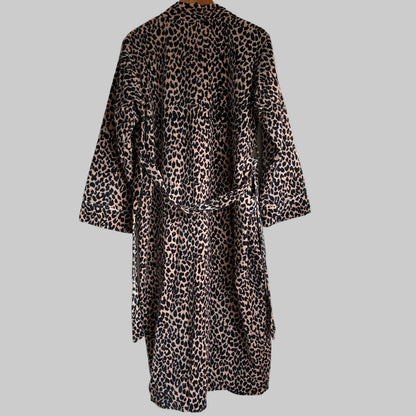A leopard print robe hanging on a hanger against a plain white wall. 
