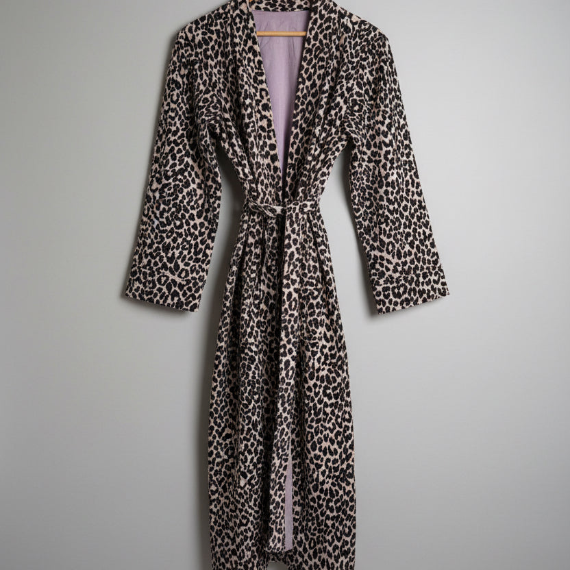 A leopard print robe hanging on a hanger against a plain white wall. 