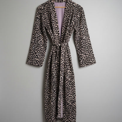 A leopard print robe hanging on a hanger against a plain white wall. 