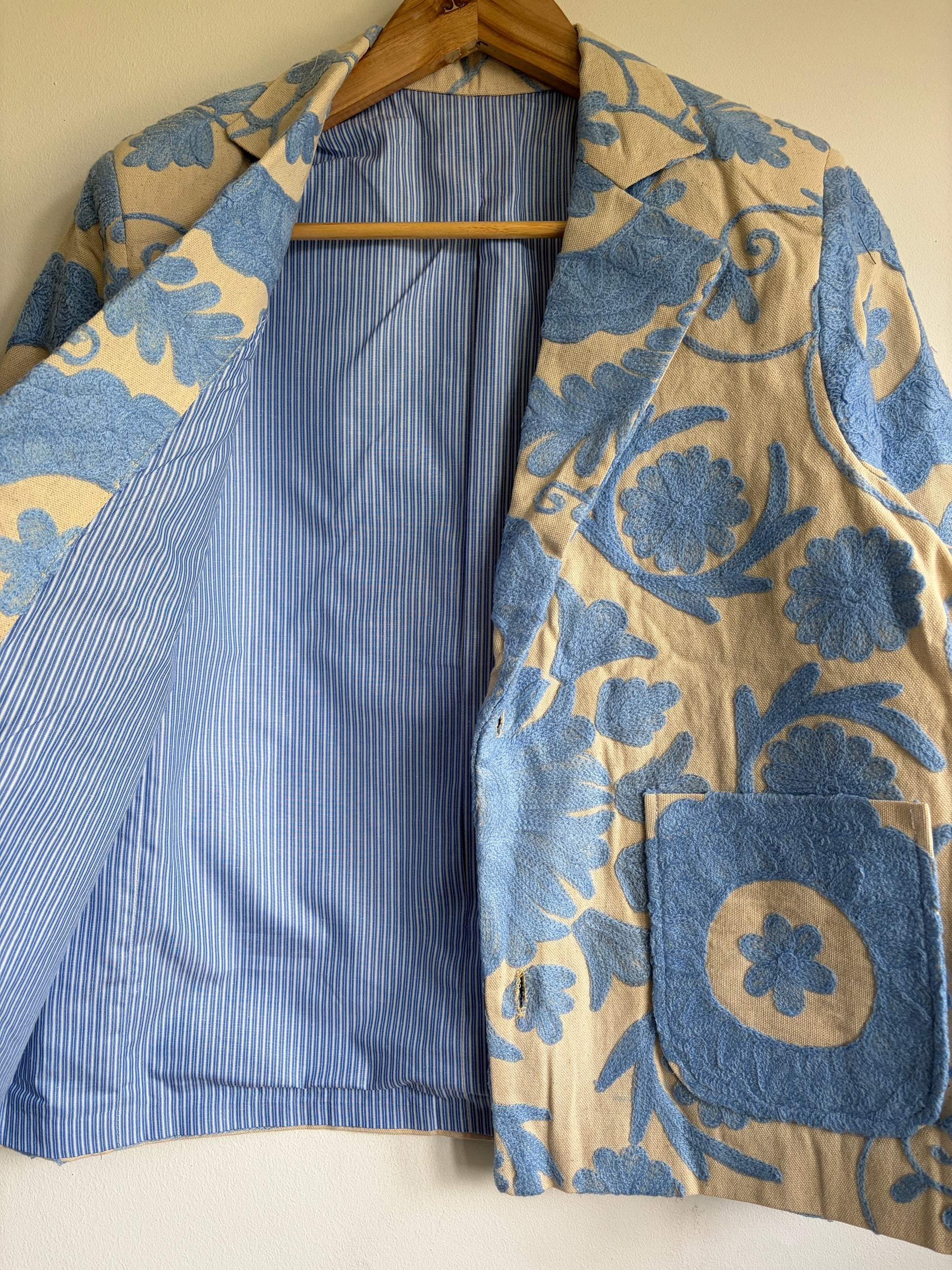 Floral-patterned jacket with blue accents on a hanger against a neutral background