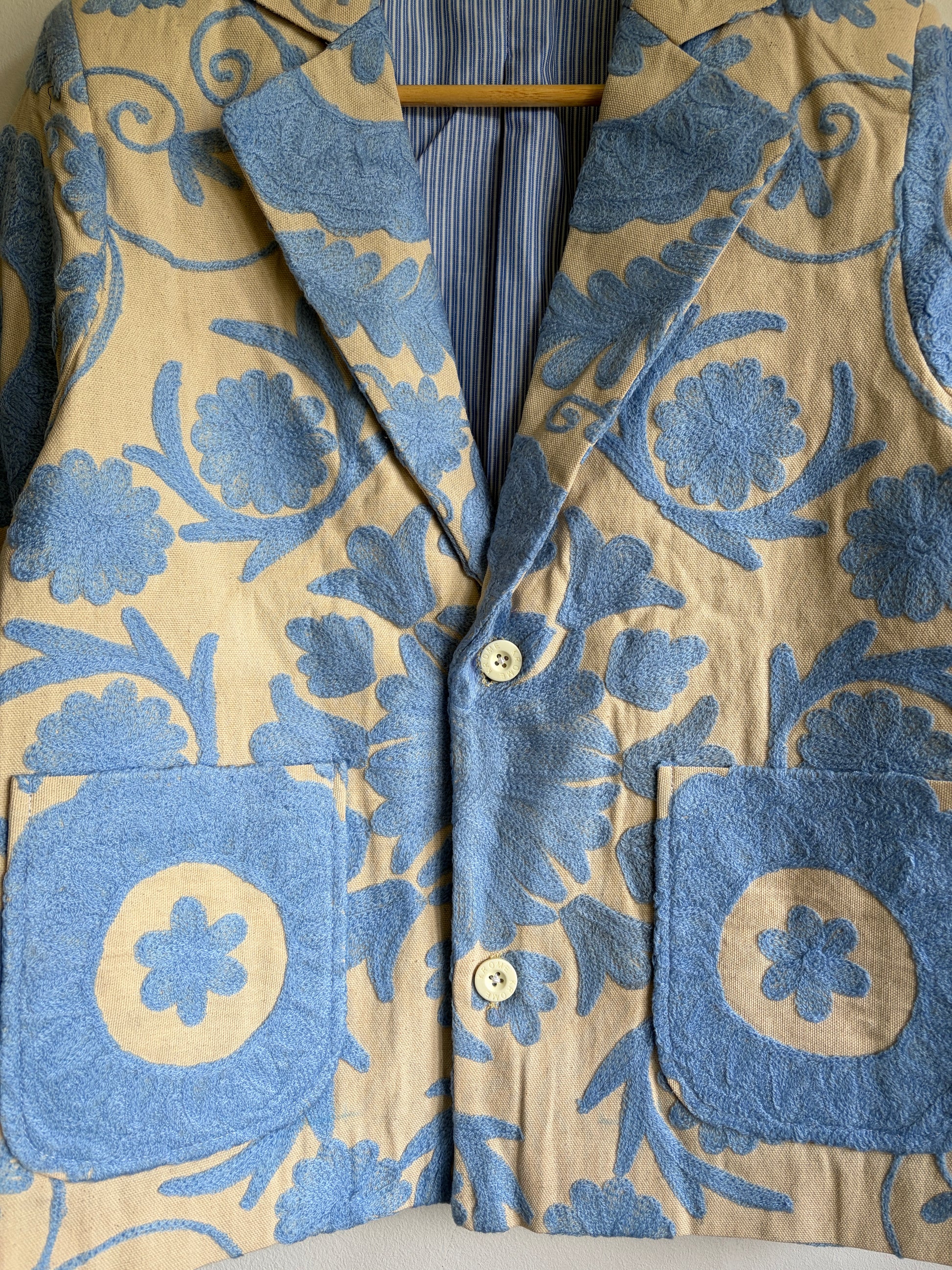 Close-up of a Suzani Floral Blazer with blue floral designs on a beige background