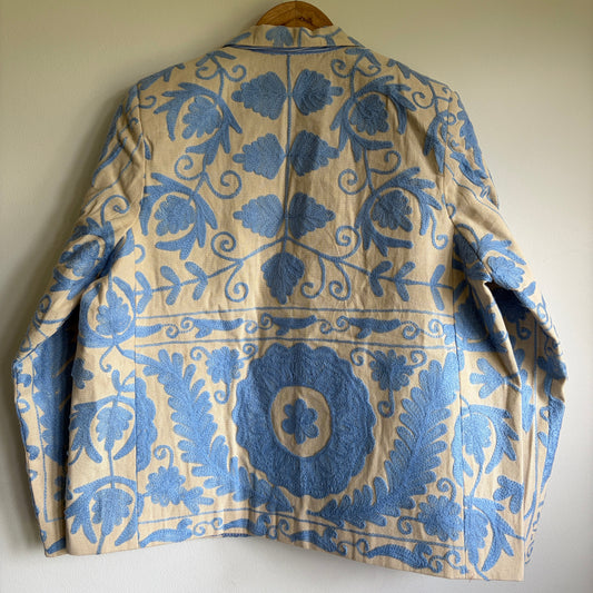 Floral patterned suzani jacket on a hanger against a plain wall