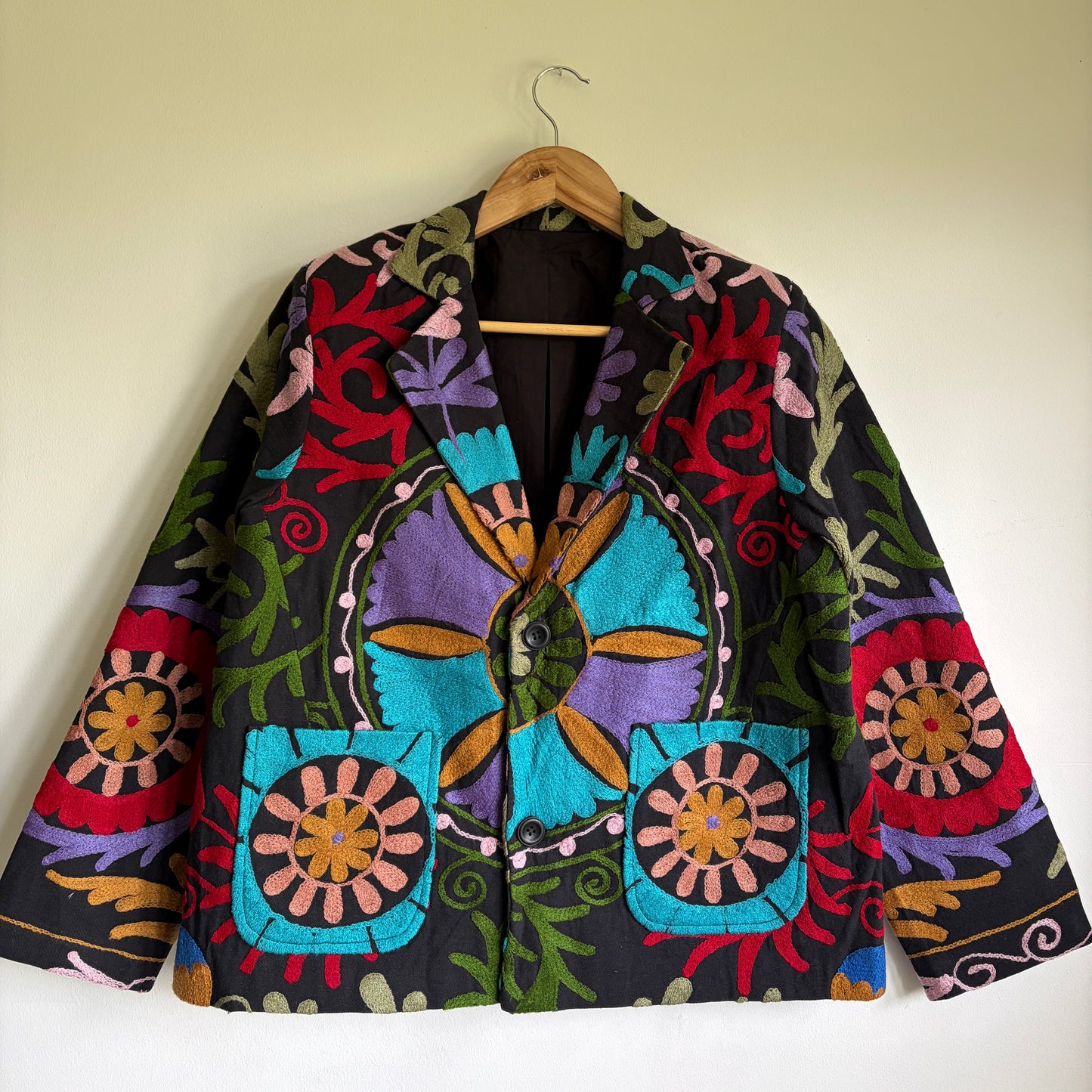 Colorful embroidered jacket on a hanger against a plain wall