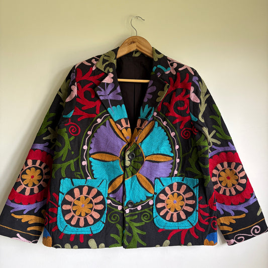 Colorful embroidered jacket on a hanger against a plain wall