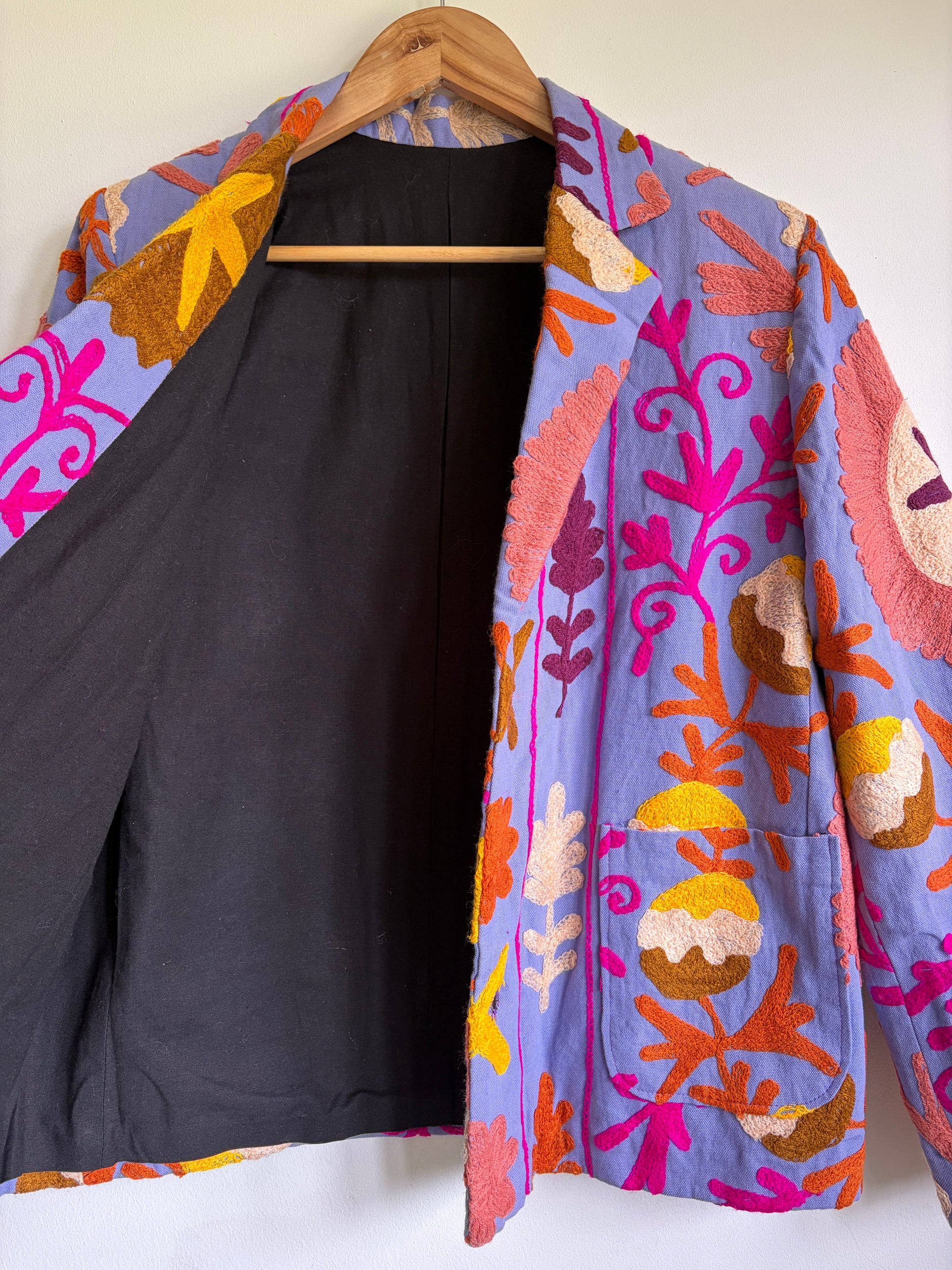Colorful embroidered jacket on a hanger against a white background