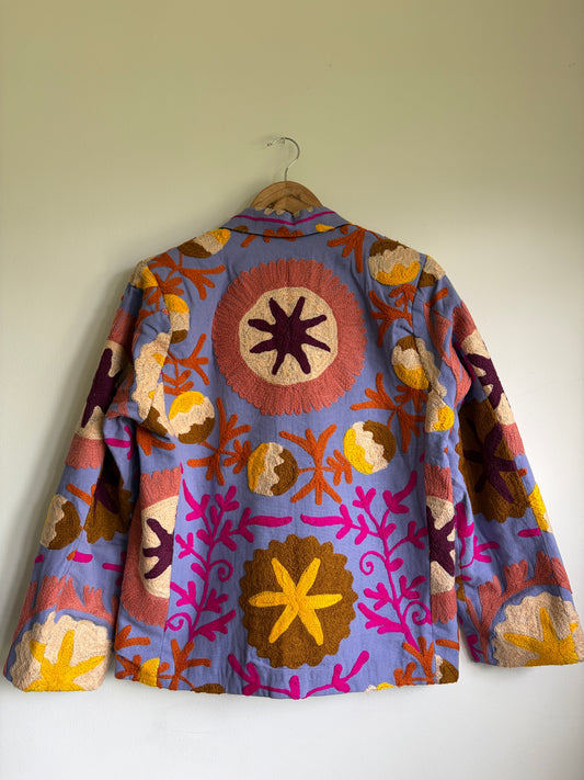 Colorful embroidered jacket on a hanger against a plain wall