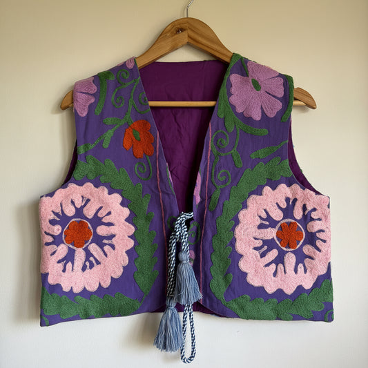 Colorful embroidered vest with floral patterns on a wooden hanger against a plain background
