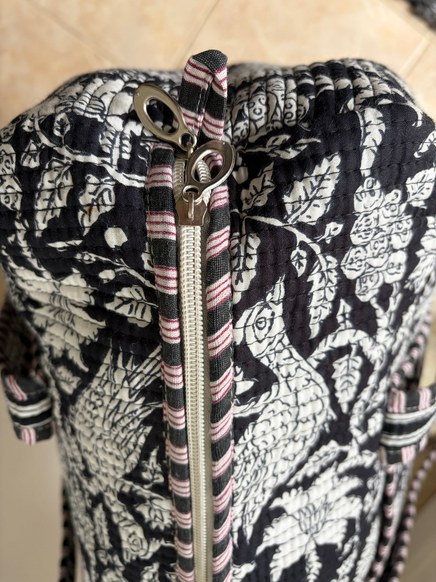 Black and white floral patterned bag with a zipper on a beige background