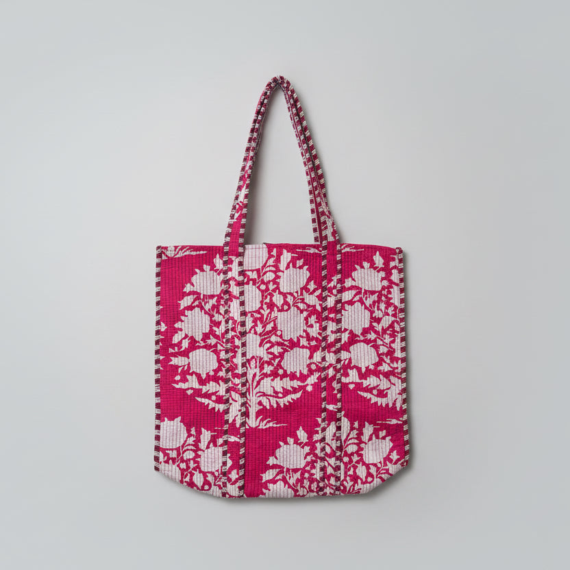 Pink and white patterned bag on a white surface with green leaves.