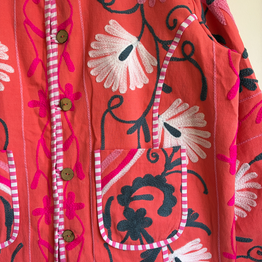 A coral pink embroidered jacket with floral and scroll patterns. 