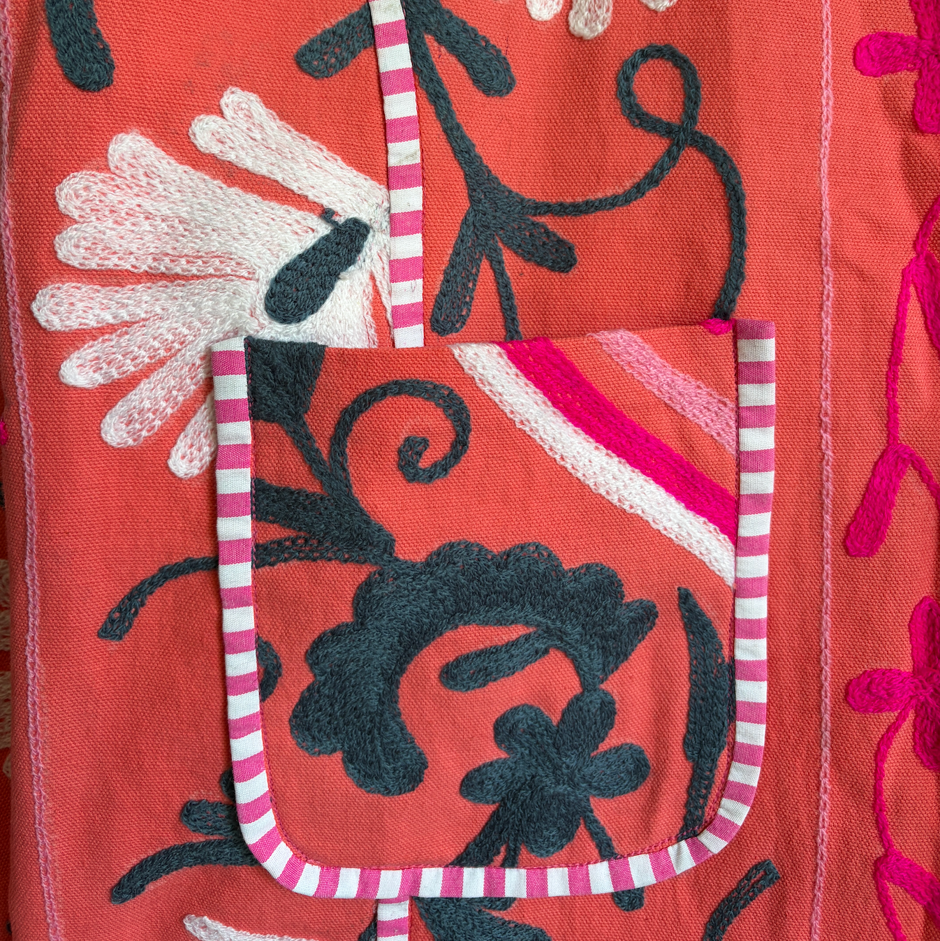 A coral pink embroidered jacket with floral and scroll patterns. 