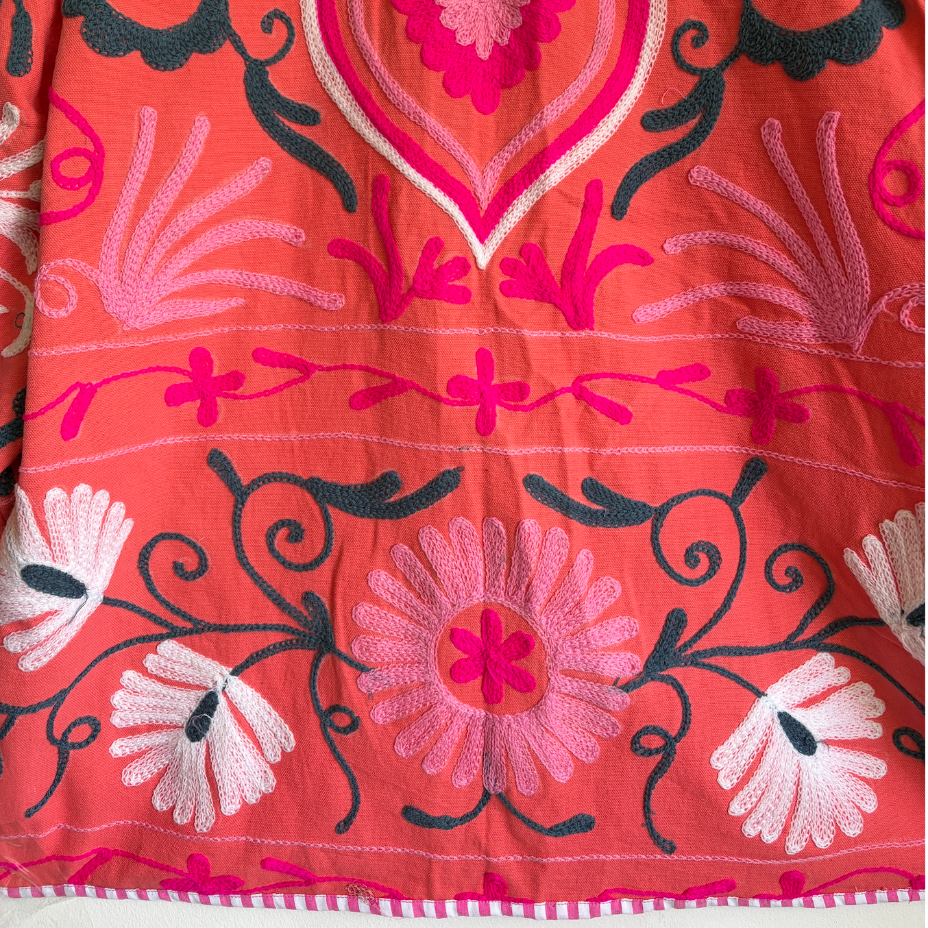 A coral pink embroidered jacket with floral and scroll patterns. 