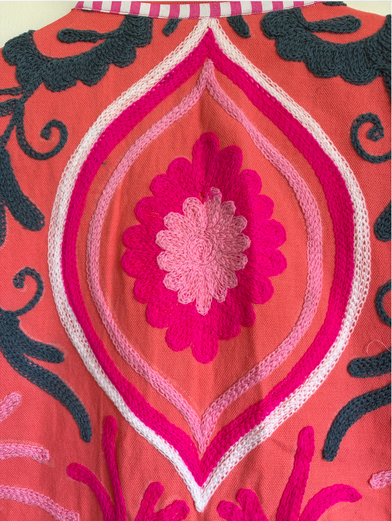 A coral pink embroidered jacket with floral and scroll patterns. 