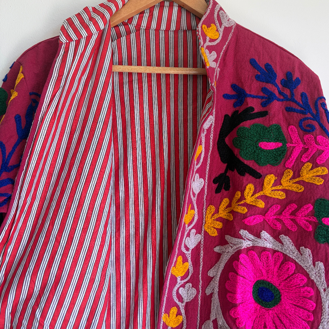 Colorful embroidered jacket on a hanger against a white background