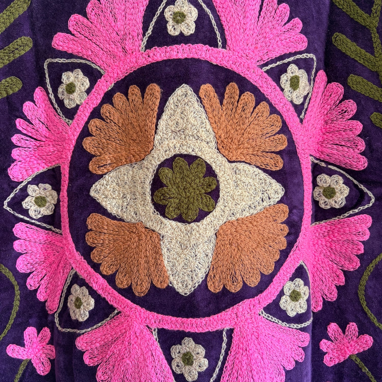 Close-up of intricate embroidery with pink, orange, and green patterns on a dark background.